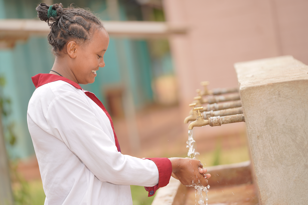 A woman in Ethiopia washes her hands with clean water using outside taps.