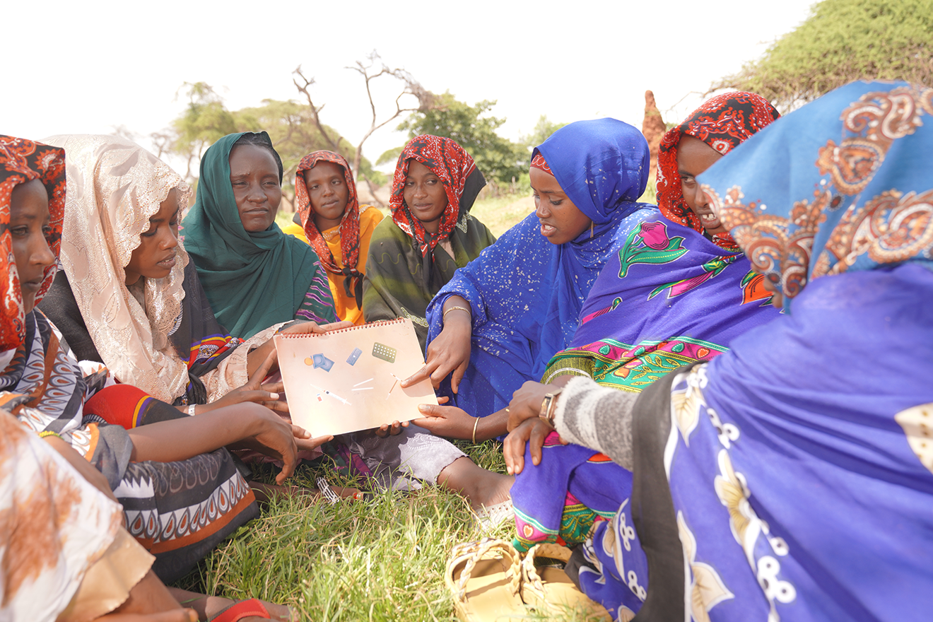 A group of women in Ethiopia sit in a circle looking at an informational sheet on contraceptives/birth control options.