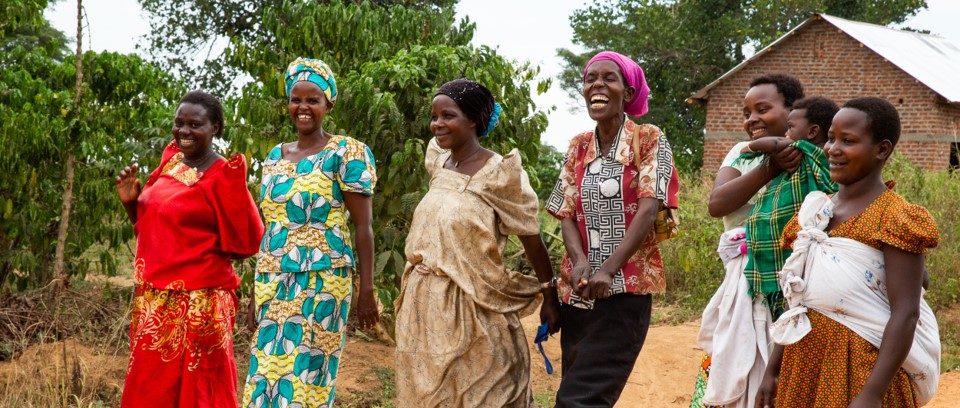 Six women stand in a line outside. One woman holds a child.