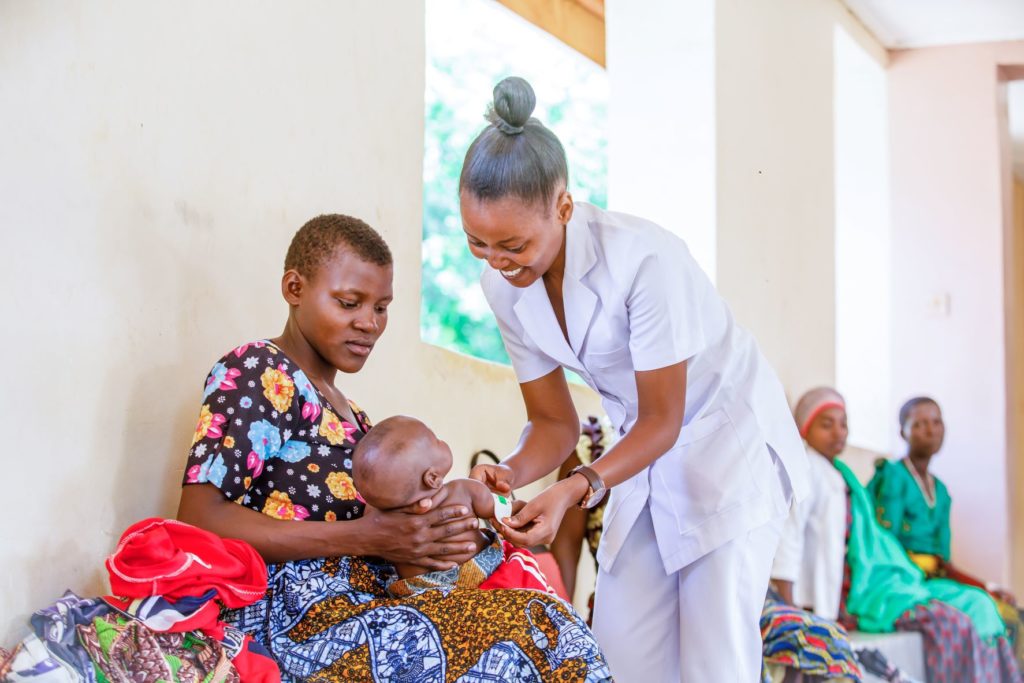 A mother holds a baby as a healthcare worker measures the baby's arm