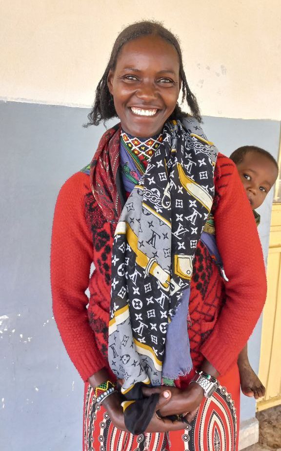 Smiling woman in a red sweater and colorful scarf with a baby on her back in Ethiopia
