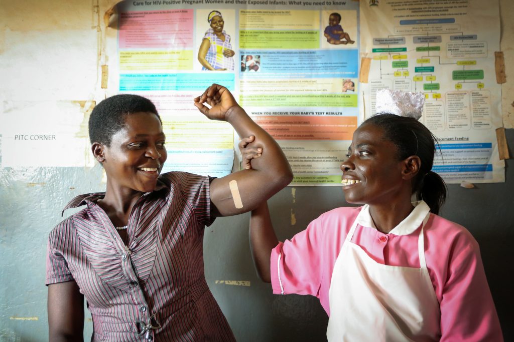 Two smiling women in a clinic, one with a bandaid on her arm