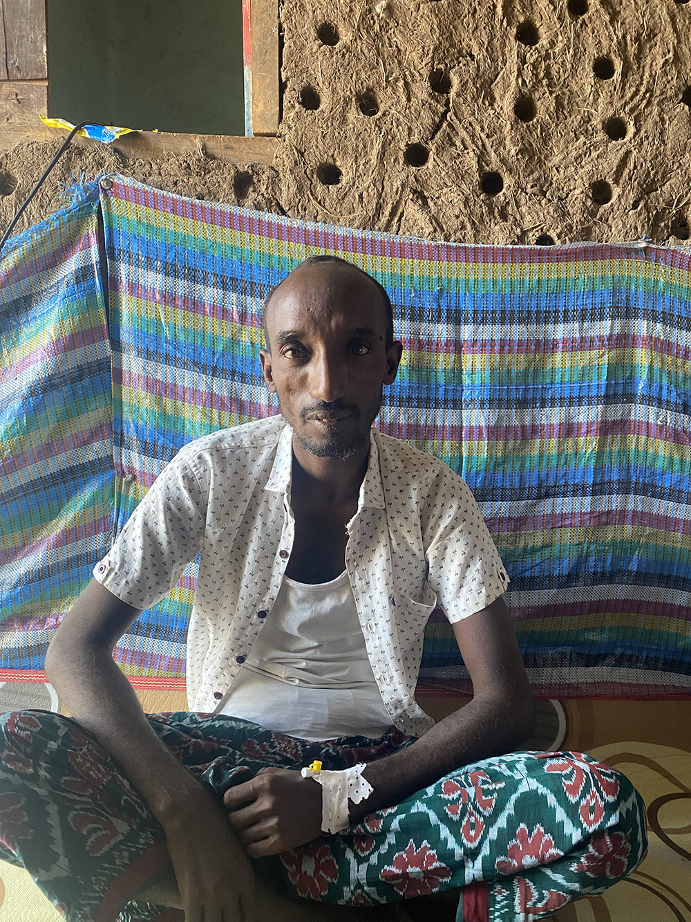 Ibrahim Meo, an Ethiopian man, sits in front of his home.