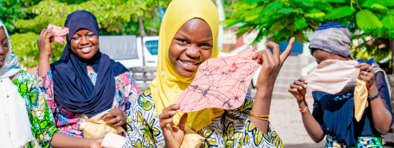 A smiling girl holds up a menstrual pad she learned to make through an EngenderHealth training.