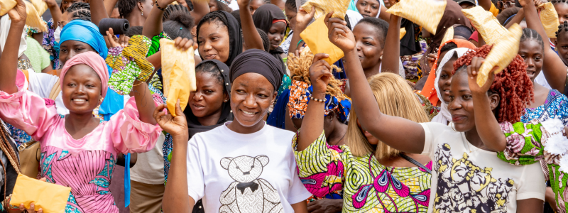 Crowd of young women and girls hold up menstrual pads and other period products in celebration after an EngenderHealth training.