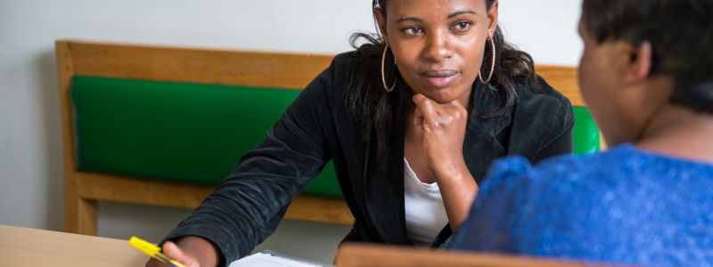 Two women speak to each other across a desk in Tanzania.