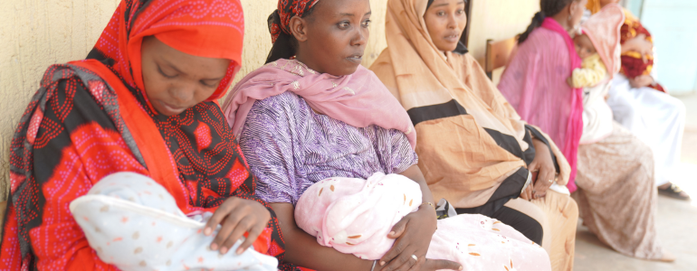 Line of mothers sit with their newborns in front of a health clinic in Ethiopia.