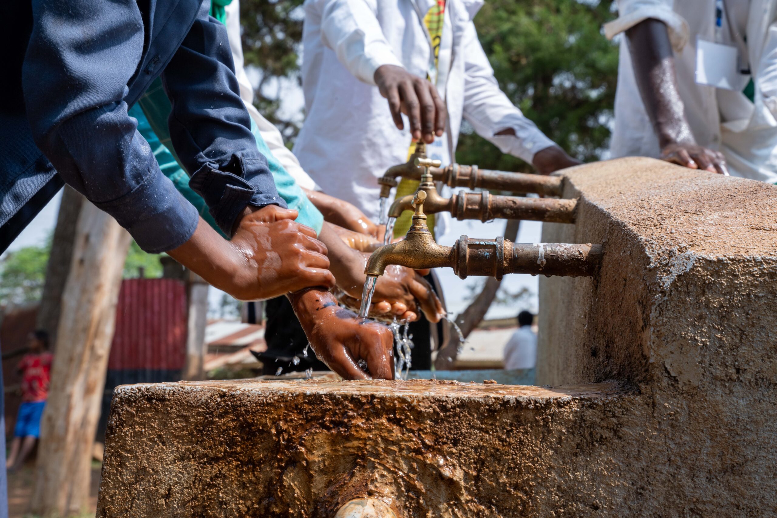 A group of young people wash their hands at a set of outdoor sinks in rural Ethiopia.