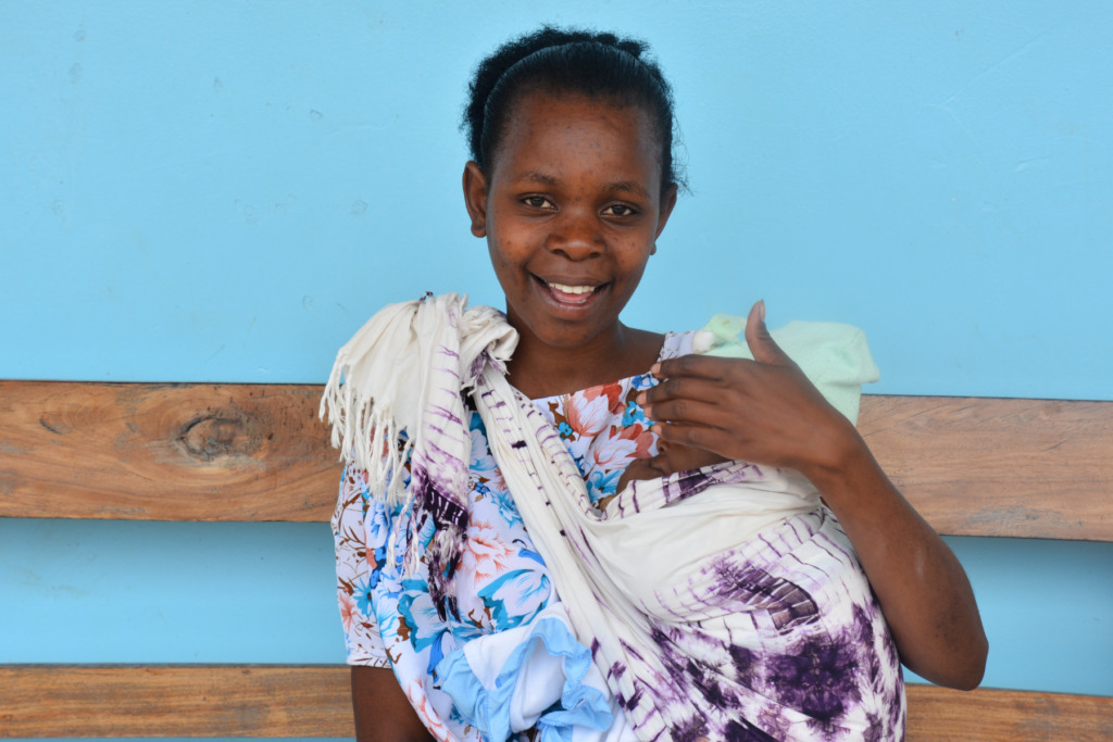 Tanzanian mother holds her baby against a blue background at health facility